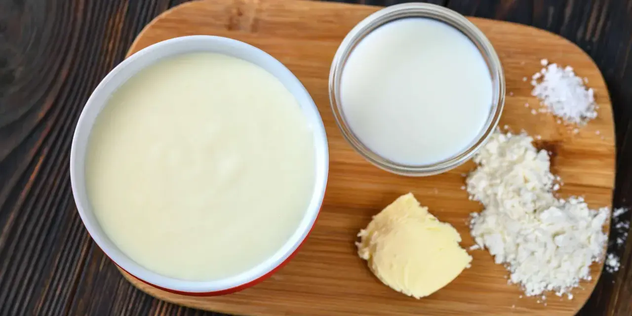 Zutaten für eine Mehlschwitze: Butter, Mehl, Milch und Salz auf einem Holzbrett.