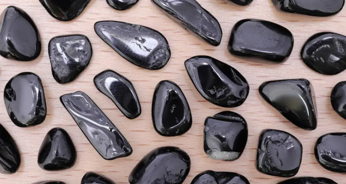 Tormalina nera, nota per le sue proprietà protettive e di radicamento, in una collezione di pietre levigate su fondo di legno.