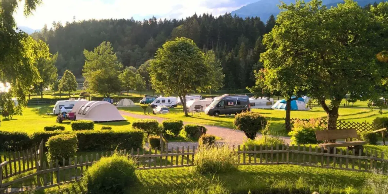 Idyllischer Campingplatz in den Dolomiten mit Wohnmobilen, Zelten und einem Teich.