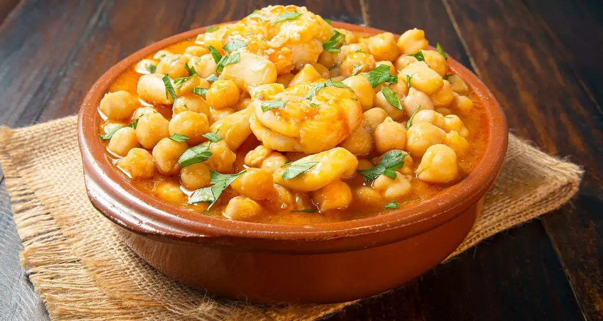 Un plato de barro con garbanzos y langostinos, adornado con perejil fresco, sobre una mesa de madera rústica.