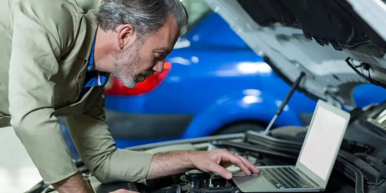 Mechanik z laptopem przy otwartej masce samochodu.