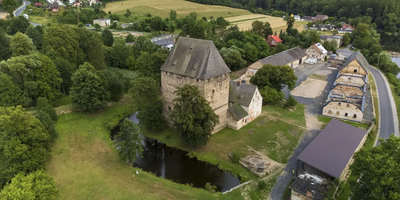 Wieża w Siedlęcinie, otoczona zielenią i stawem, góruje nad okolicą. W tle widać zabudowania i pagórkowaty krajobraz.