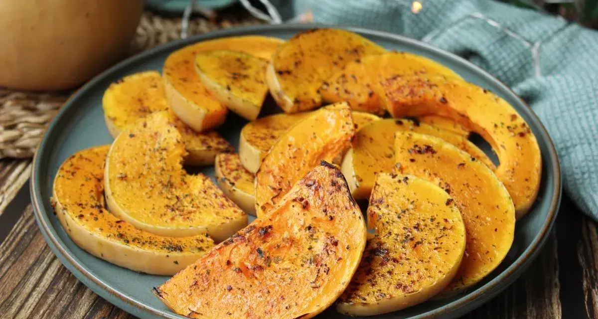 Rodajas de calabaza a la plancha, doradas y especiadas, servidas en un plato azul sobre una mesa de madera.