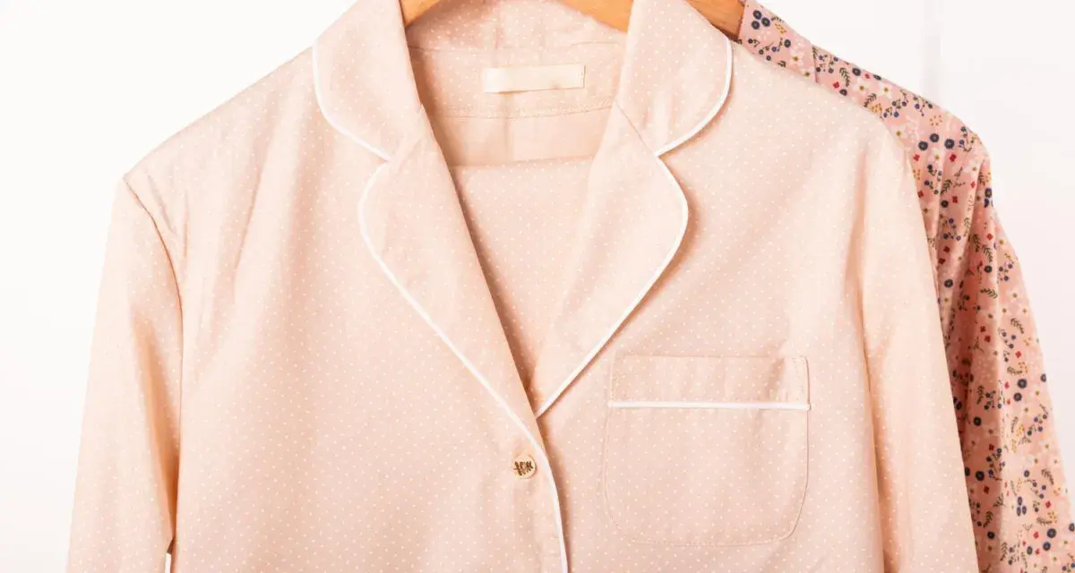 Pyjama rose à pois blancs, col rabattu, suspendu sur un cintre en bois. Une autre chemise à fleurs est visible derrière.