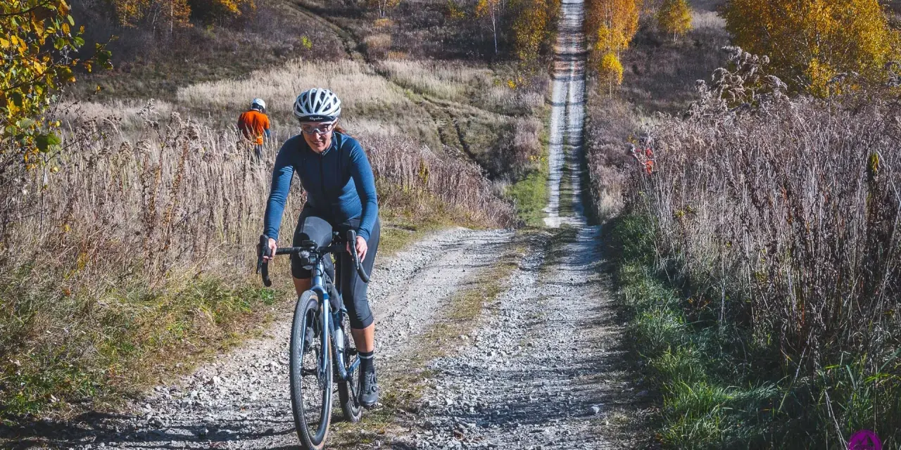 Kobieta na rowerze pokonuje kamienistą drogę w Dolinkach Krakowskich. Jesienne liście i wysoka trawa tworzą malowniczy krajobraz.