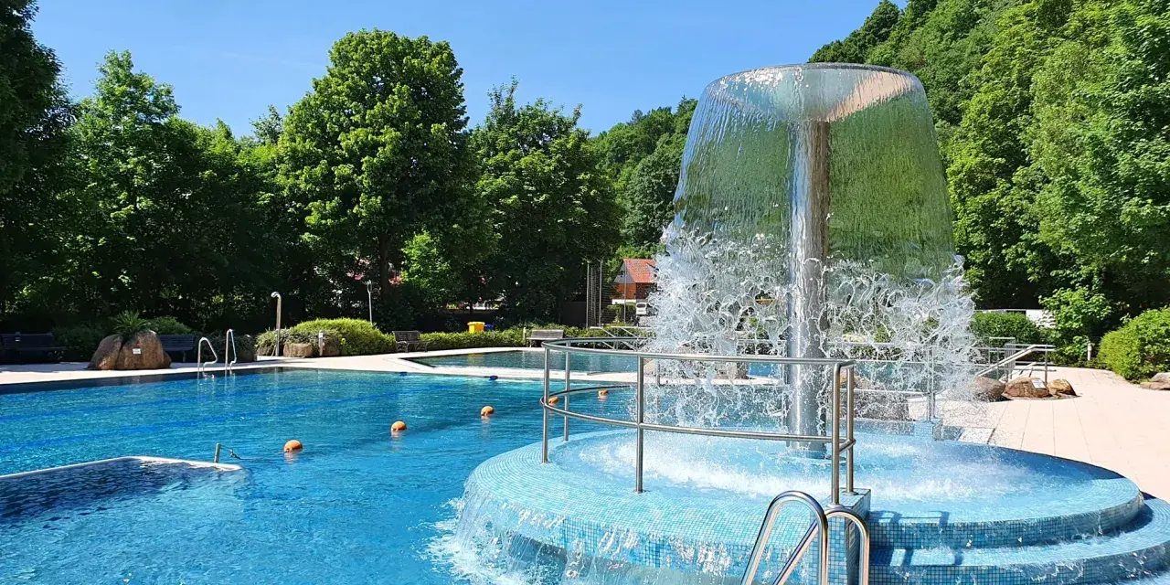 Erfrischender Brunnen im Naturbad Elbingerode, umgeben von grünen Bäumen und blauem Wasser.