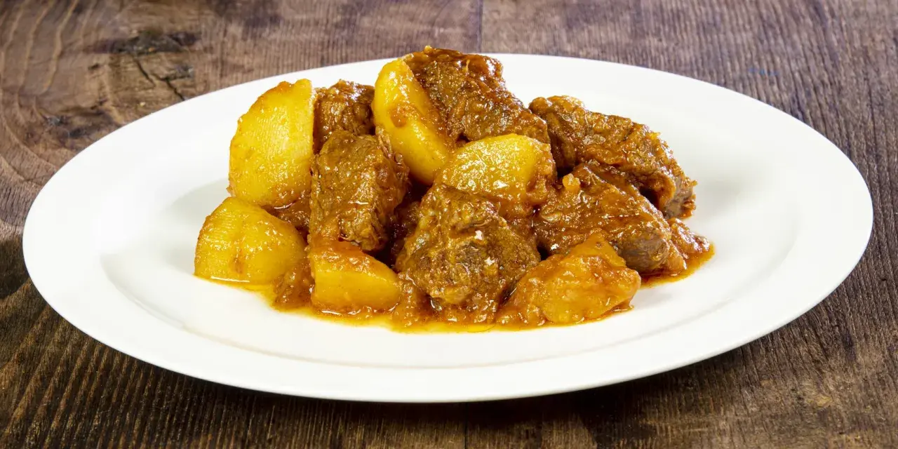 Un saporito spezzatino di vitello con patate, servito su un piatto bianco, su uno sfondo di legno scuro.