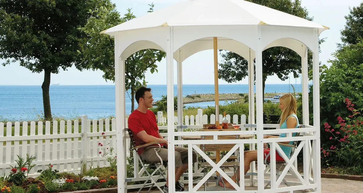 Ett par njuter av utsikten vid havet under en vit paviljong. Perfekt för att bygga paviljong och skapa en avkopplande oas.
