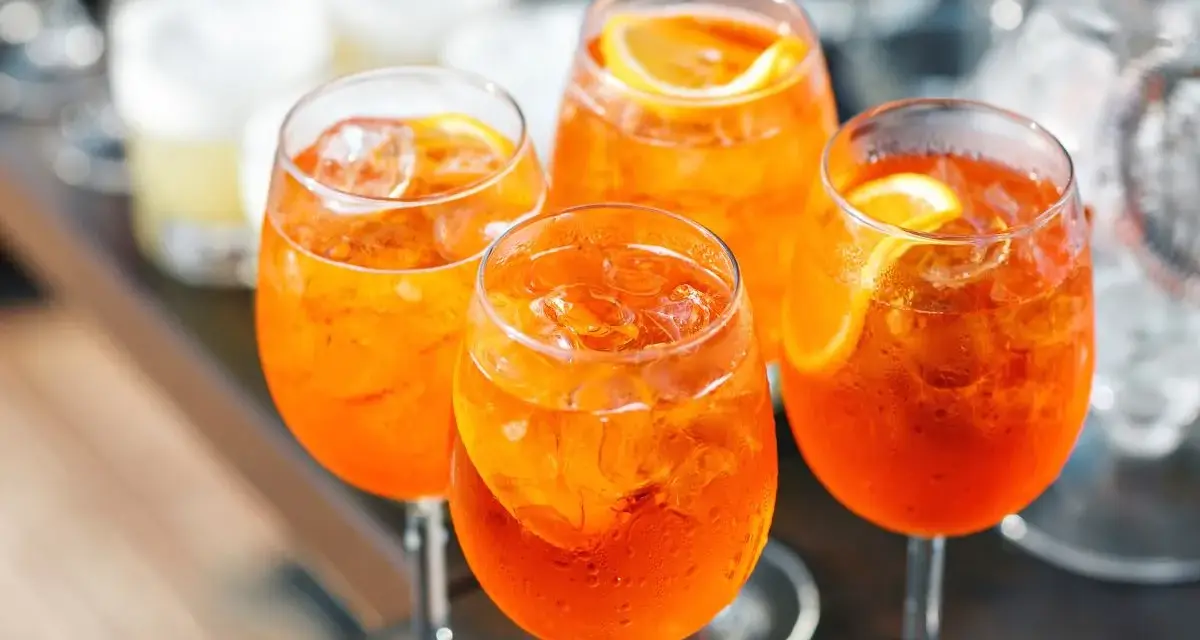 Cztery orzeźwiające drinki Aperol z lodem i plasterkiem pomarańczy, gotowe do degustacji.