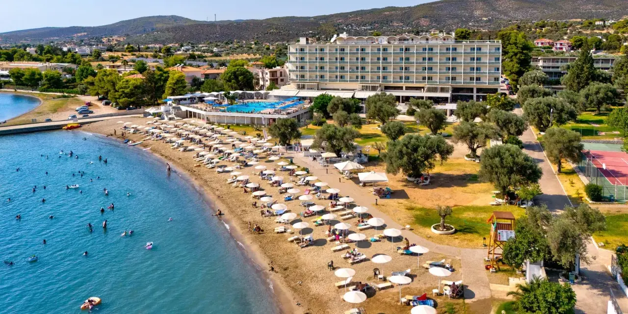 Piękna plaża na Evii, idealna na wycieczki fakultatywne. Hotel, basen, leżaki i mnóstwo ludzi kąpiących się w morzu.