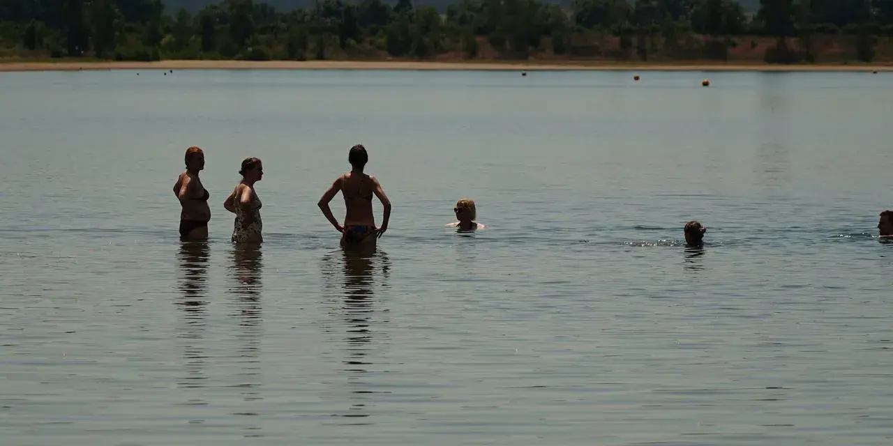 Menschen genießen das naturbad luppa an einem sonnigen Tag. Einige stehen im Wasser, andere schwimmen.