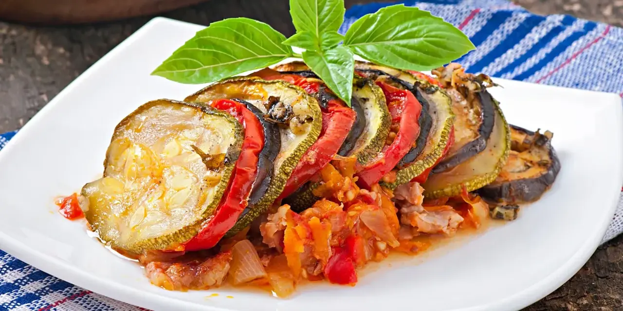 Ratatouille con rodajas de calabacín, berenjena y tomate, decorado con albahaca. Los ingredientes ratatouille se ven tiernos y jugosos.