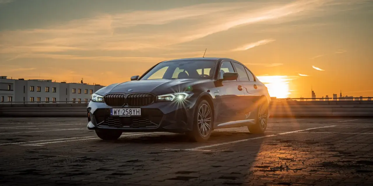 Ciemnoszara limuzyna BMW 330e na parkingu o zachodzie słońca.
