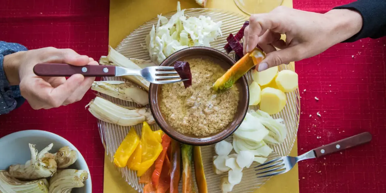 Un gruppo di mani intinge verdure nella bagna cauda, un piatto conviviale.