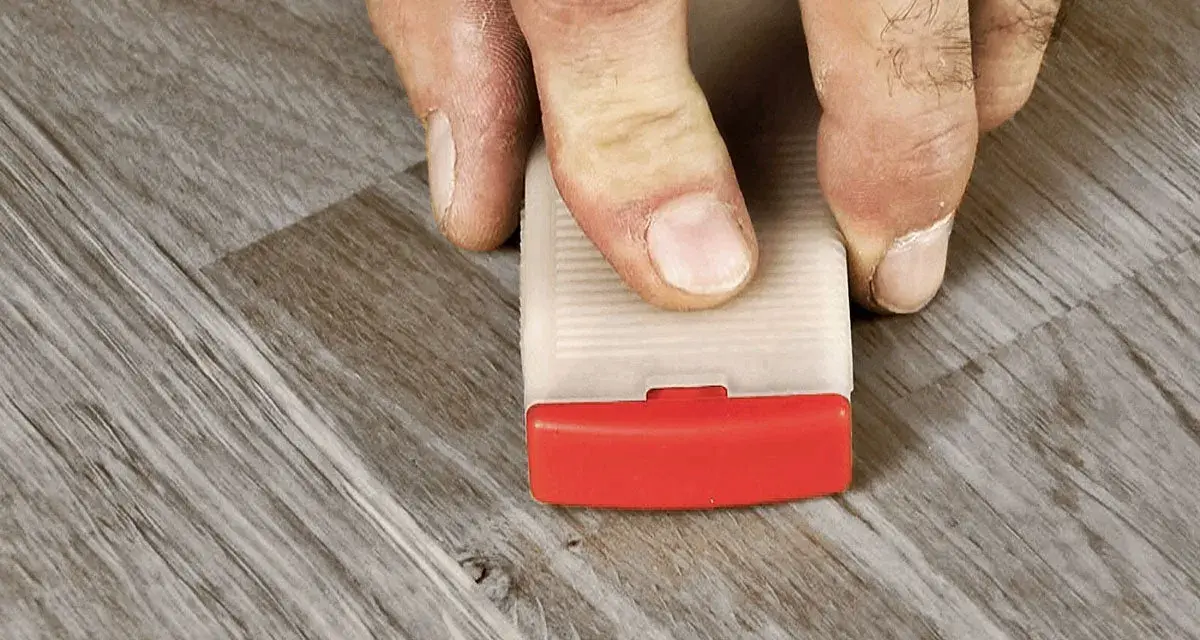 Fingrar använder en kil för att laga laminatgolv.
