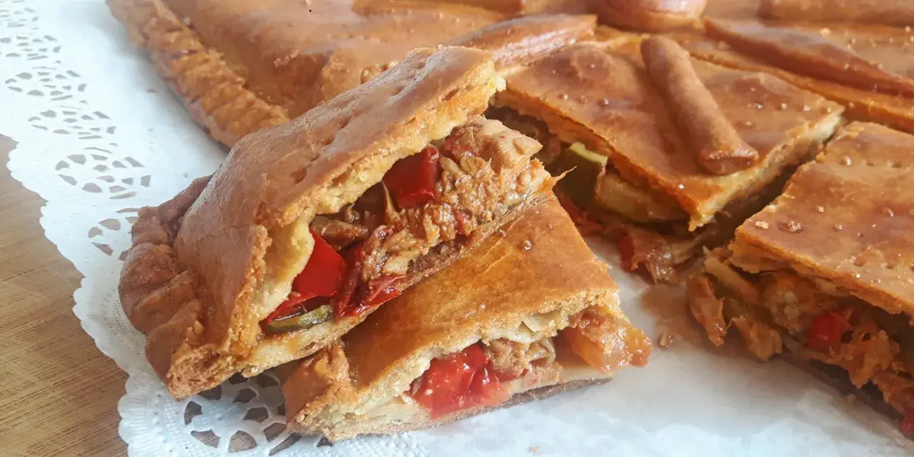 Una deliciosa empanada de carne, cortada en porciones, revela su jugoso relleno de carne deshebrada y pimientos rojos.