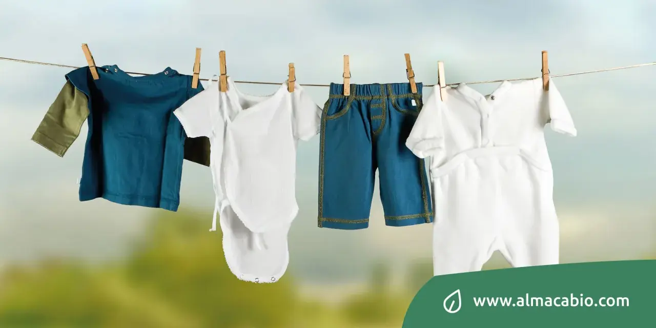 Baby clothes hanging on a clothesline: a blue long-sleeve shirt, a white onesie, blue shorts, and a white romper.