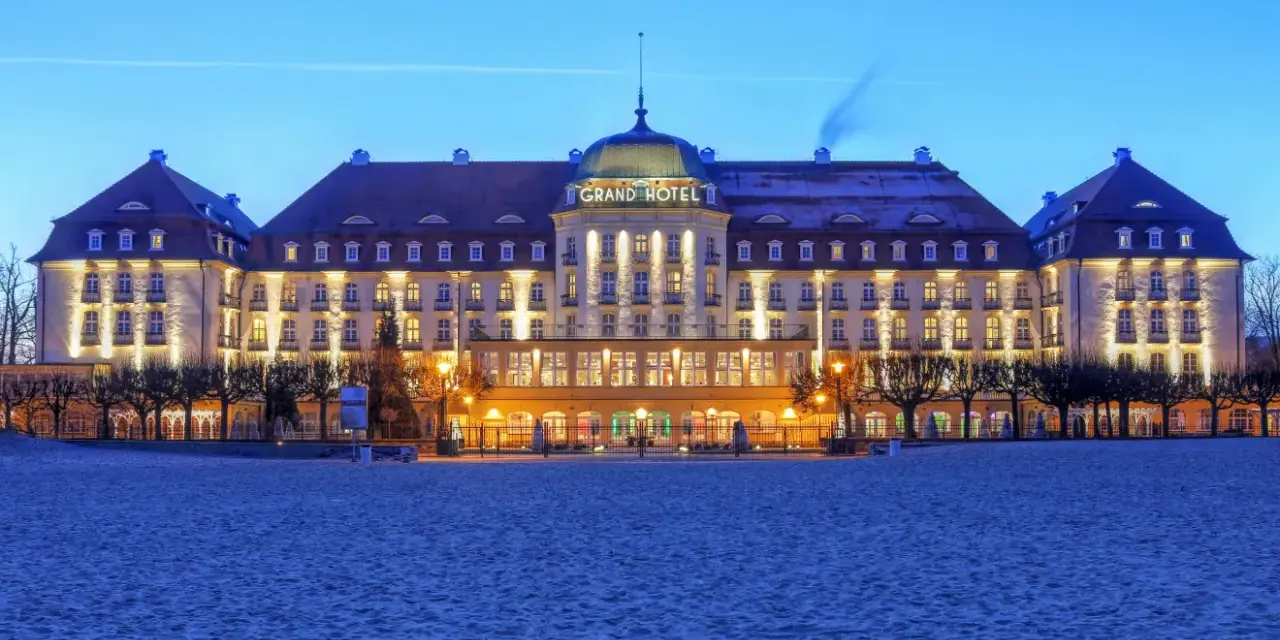 Elegancki Grand Hotel, część sieci luksusowych hoteli, lśni nocą na tle plaży.