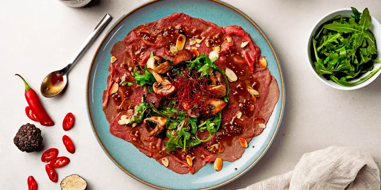 Carpaccio vom Rind mit Pilzen, Rucola und Mandeln, garniert mit Chili und Trüffel. Ein Gericht, das zeigt, was ist Carpaccio.