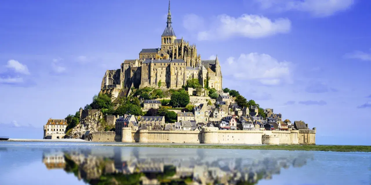 Opactwo Mont Saint-Michel, jeden z najpiękniejszych miejsc we Francji, odbija się w spokojnej wodzie.