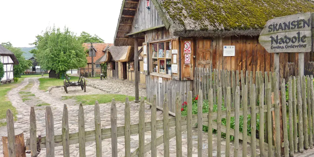 Drewniane chaty ze słomianymi dachami w skansenie w Nadolu. W oddali widać wóz.