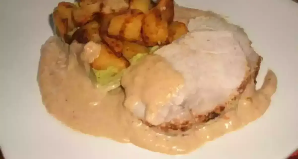 Tranche de roti de porc au lait, nappée d'une sauce onctueuse, accompagnée de pommes de terre rôties croustillantes. Un plat réconfortant.