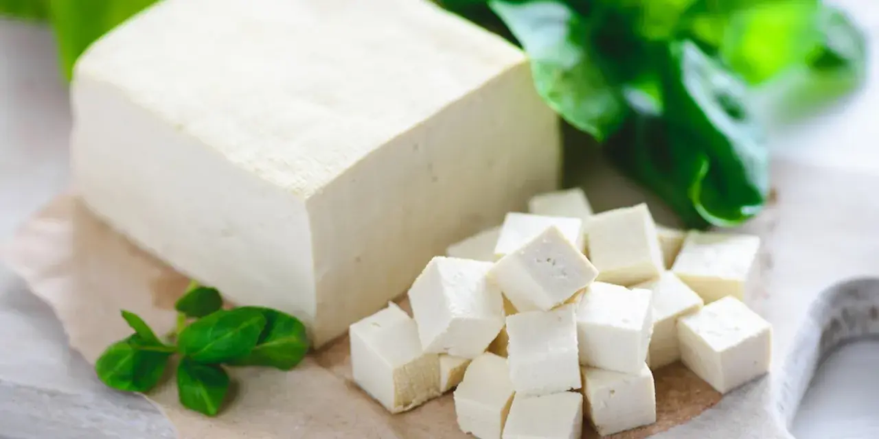 Kostka tofu, z czego jest zrobione, pokrojona w kostkę i ozdobiona listkami bazylii.