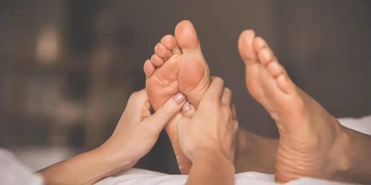 Hands giving a relaxing foot rub to a person lying on a white surface.