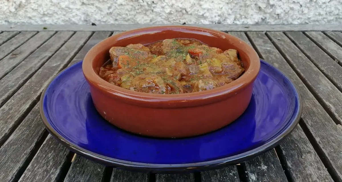 Goulash de ternera humeante en cazuela de barro, servido sobre plato azul. Un plato reconfortante listo para disfrutar.