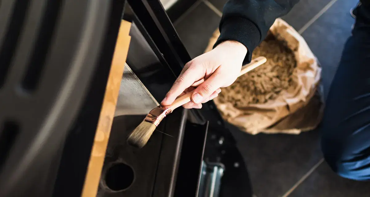 Mano che pulisce la stufa a pellet con un pennello. La manutenzione stufa a pellet ogni quanto è fondamentale per l'efficienza.