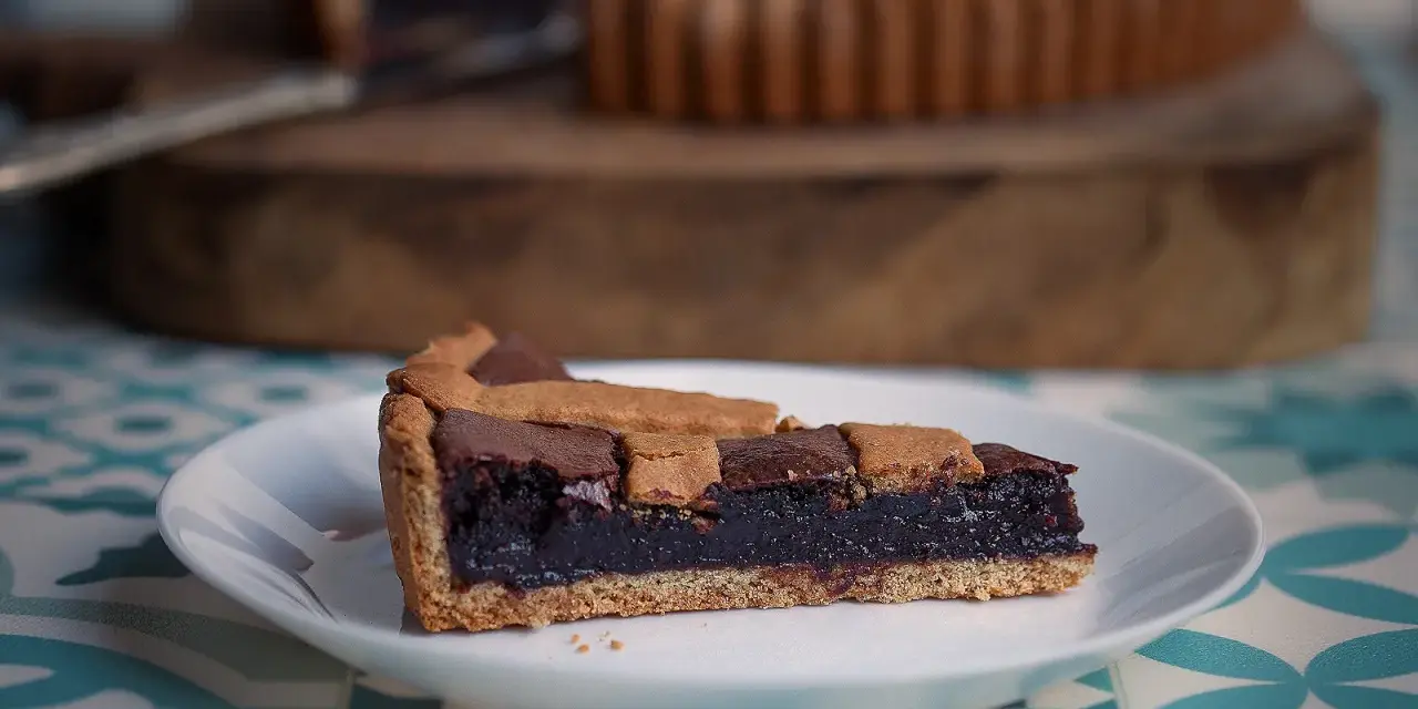 Una fetta di crostata al cioccolato, con la sua base dorata e il ripieno scuro e invitante, pronta per essere gustata.
