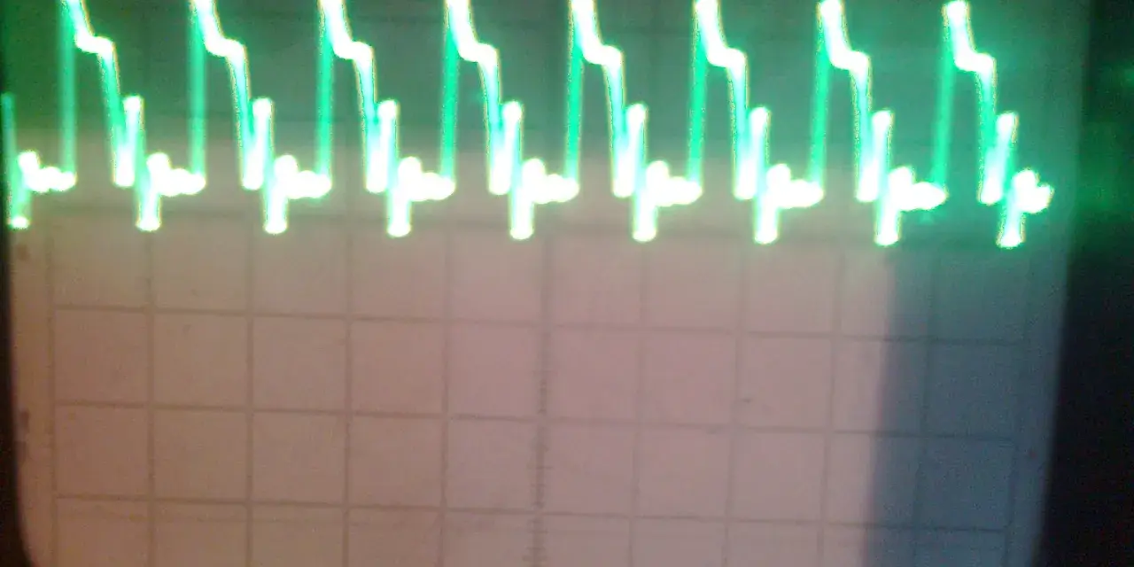 Zielone, kwadratowe fale na ekranie oscyloskopu, przypominające schody.