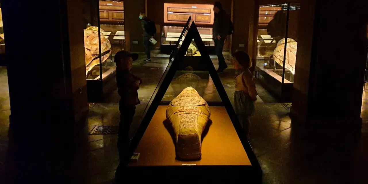 W muzeum archeologicznym w Krakowie dzieci oglądają starożytną mumię w sarkofagu.