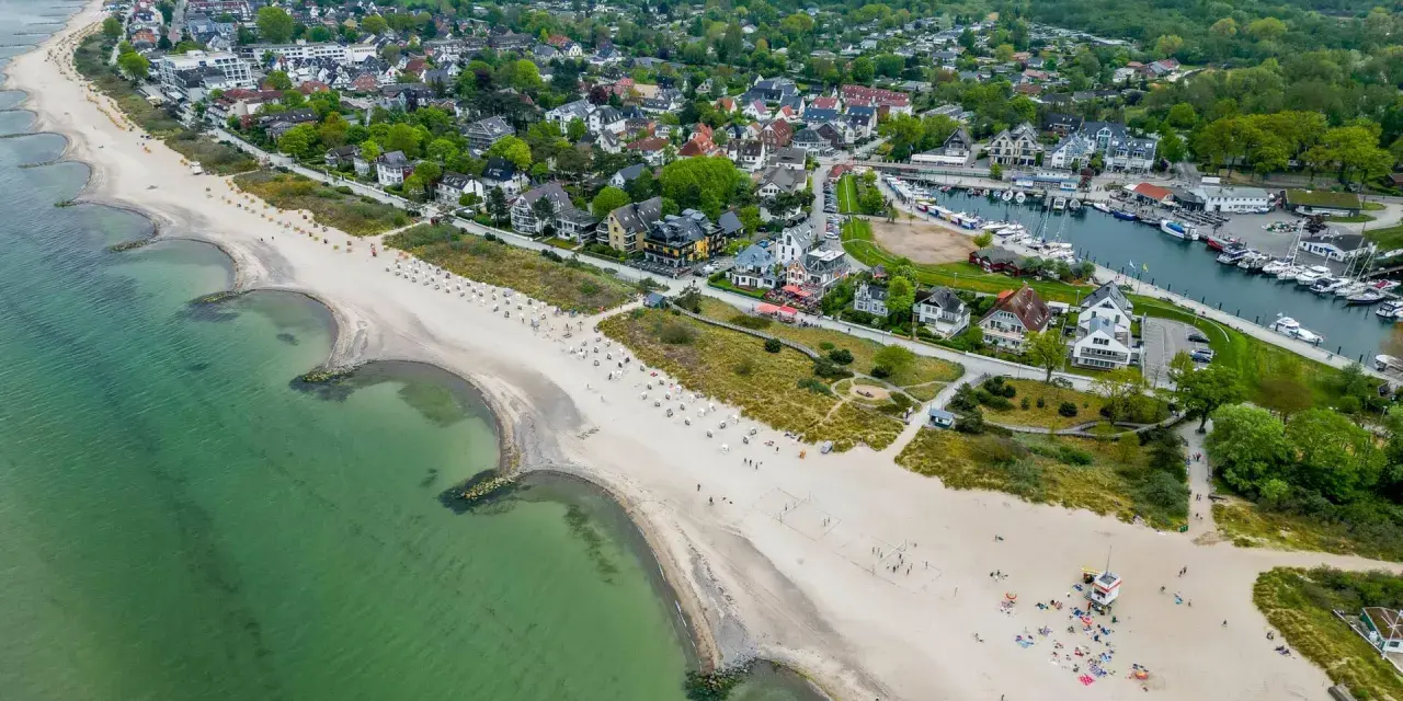 Luftaufnahme eines Strandes mit grüner Ostsee, Häusern und einem Yachthafen. Ein idyllischer Ort für ruhige Orte an der Ostsee.