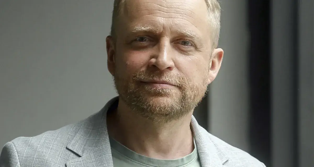 Piotr Adamczyk, znany z wielu filmów, seriali i programów, w jasnej marynarce i zielonej koszulce.