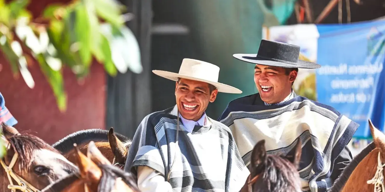 Deux huasos rient joyeusement à cheval, vêtus de ponchos traditionnels et de chapeaux.