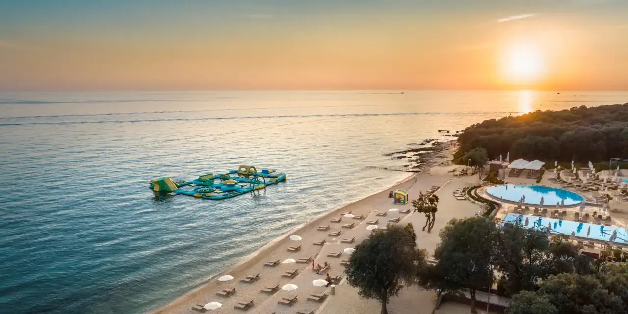 Zachód słońca nad morzem przy plaży z dmuchanym placem zabaw i basenem. Idealne miejsce na wakacje w camping Vrila.