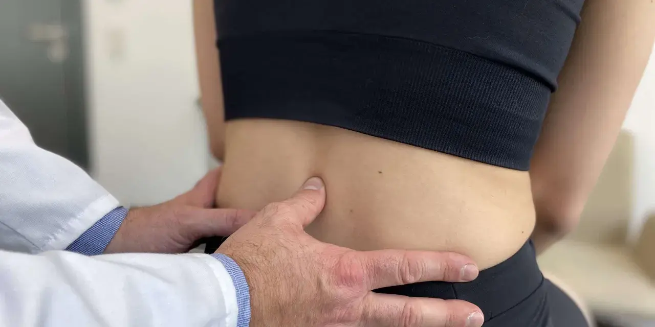 Lekarz bada odcinek lędźwiowy kręgosłupa pacjentki, oceniając objawy spondylozy lędźwiowej.