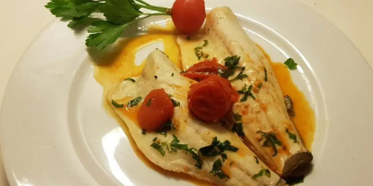 Filetti di branzino in padella con pomodorini e prezzemolo, un piatto leggero e saporito.