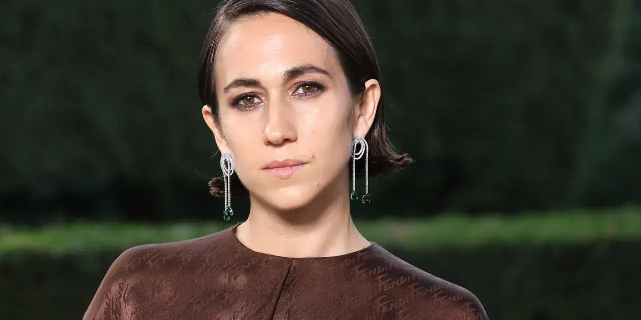 Delfina Delettrez Fendi indossa orecchini pendenti con diamanti e smeraldi, abbinati a un abito marrone con logo Fendi.