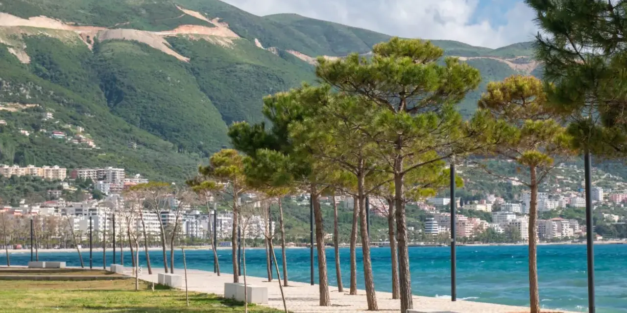 Wlora, Albania: nadmorska promenada z drzewami i widokiem na miasto u podnóża zielonych wzgórz.