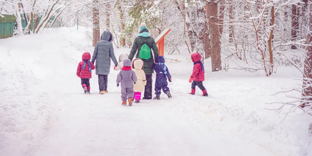 Kindergarten-Pflicht: Eine Gruppe Kinder und Erzieherinnen stapfen durch tiefen Schnee im Wald.