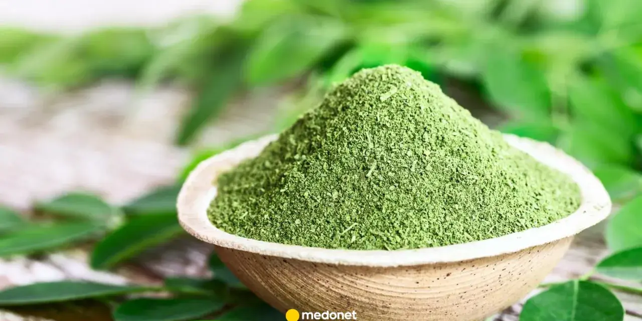Zielony proszek z liści moringa w miseczce, otoczony świeżymi liśćmi. Odkryj niezwykłe liście moringa właściwości.