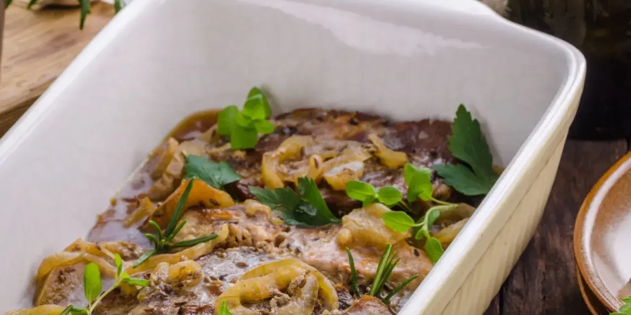 Schab pieczony w piekarniku w naczyniu, duszony z cebulą i ziołami. Aromatyczne danie gotowe do podania.