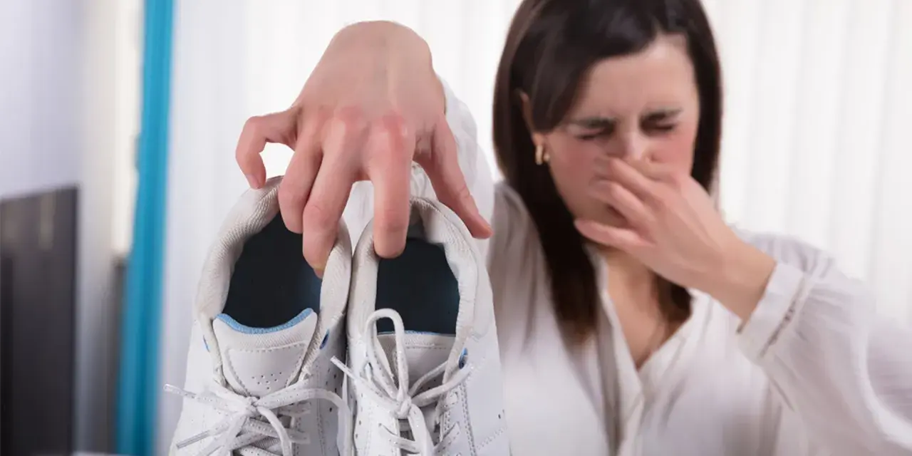 Mujer tapándose la nariz por el mal olor de sus zapatillas blancas. ¡Descubre cómo quitar el olor de los pies y de tu calzado!