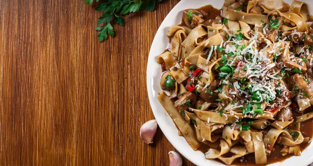 Pyszne danie z makaronem malfadine czy tagliatelle z grzybami i parmezanem, podane na drewnianym blacie.