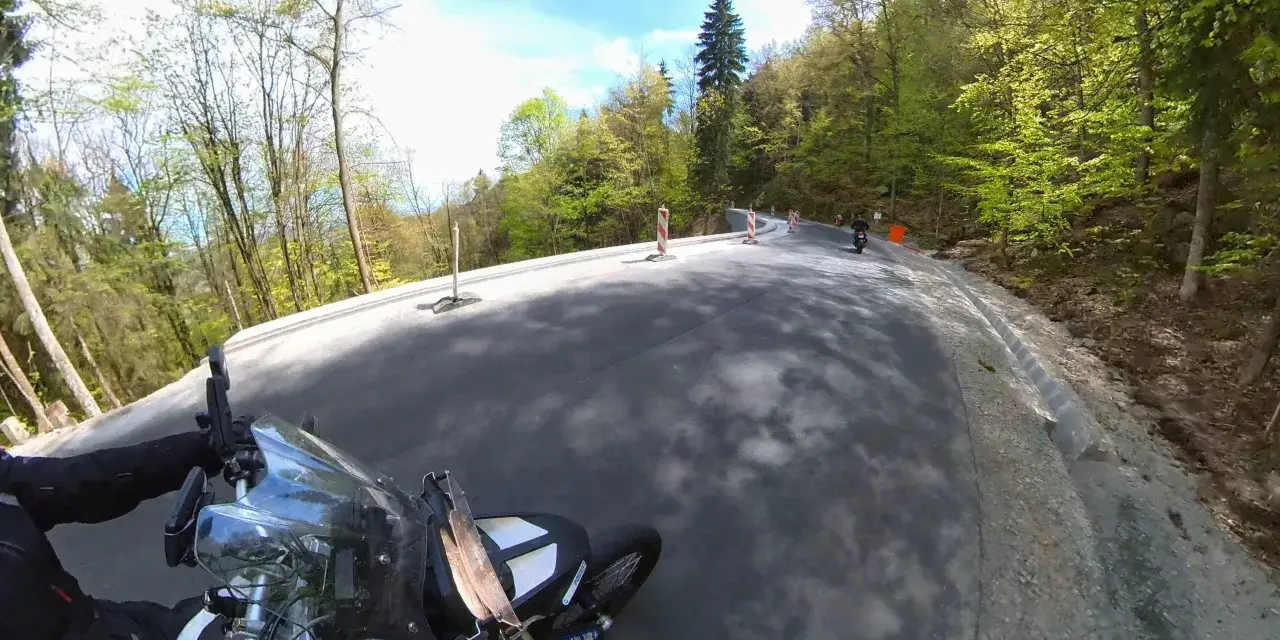Motocyklista pokonuje krętą drogę stu zakrętów, otoczoną zielonym lasem.
