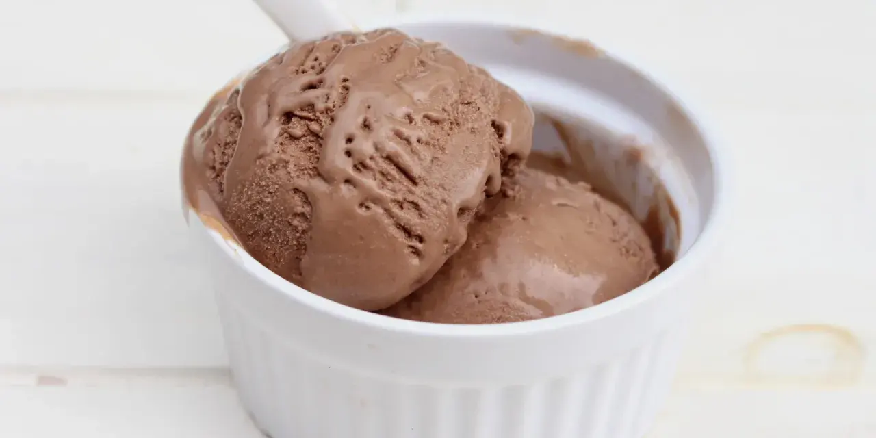 Dos bolas de cremoso helado de chocolate derritiéndose en un cuenco blanco.