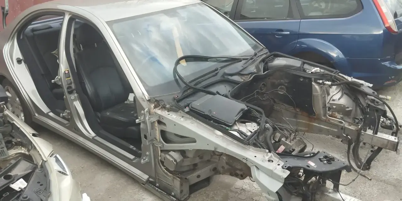 Złomowanie auta: srebrny sedan bez maski i zdemontowanymi częściami, obok niebieski kombi.