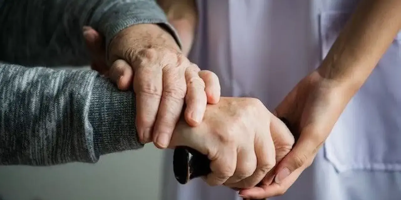 Manos de un anciano y un cuidador sujetando un bastón. Apoyo y cuidado para la dependencia.